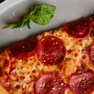 Close-up of a pepperoni pizza slice with basil garnish.
