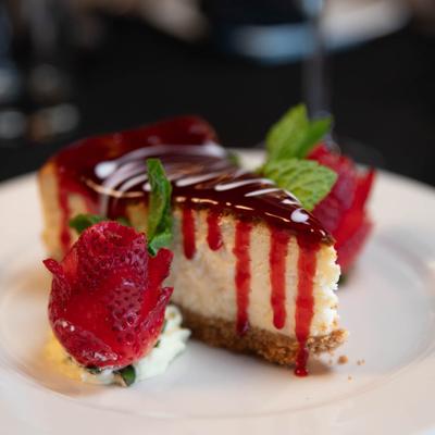 Cheesecake slice with red sauce topping, garnished with a strawberry and fresh mint leaves.