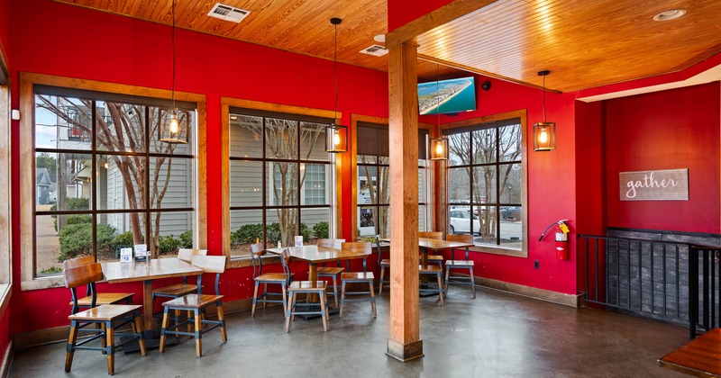 Interior of a cafe with red walls, wooden ceiling, large windows, wooden tables and chairs