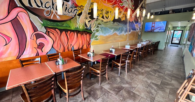 Interior dining area with lined-up wooden tables and chairs, a colorful mural on the wall