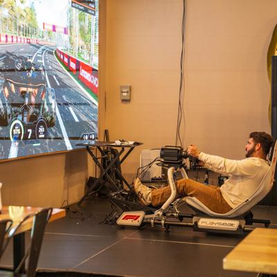 A guest drives an F1 racing simulator cockpit in front of a giant screen.