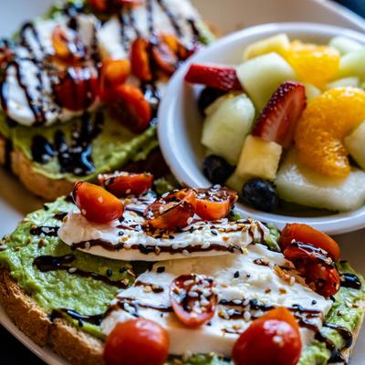 Avocado Caprese toast served with a small bowl of fruit.