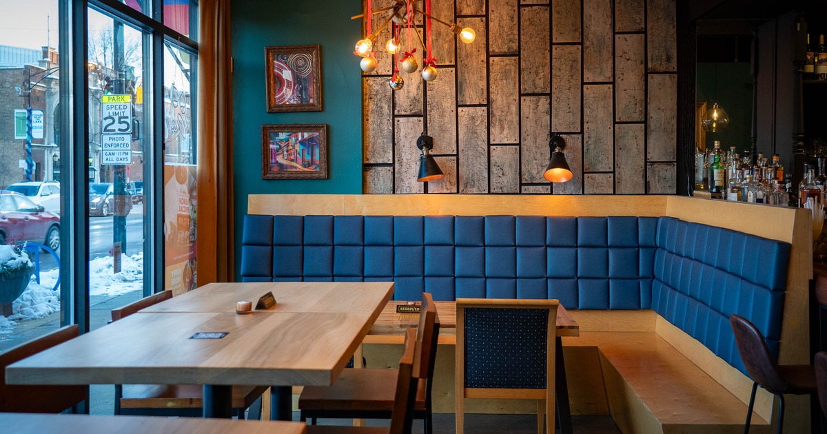 A cozy interior - wooden tables, blue upholstered booth seating and artwork on paneled walls