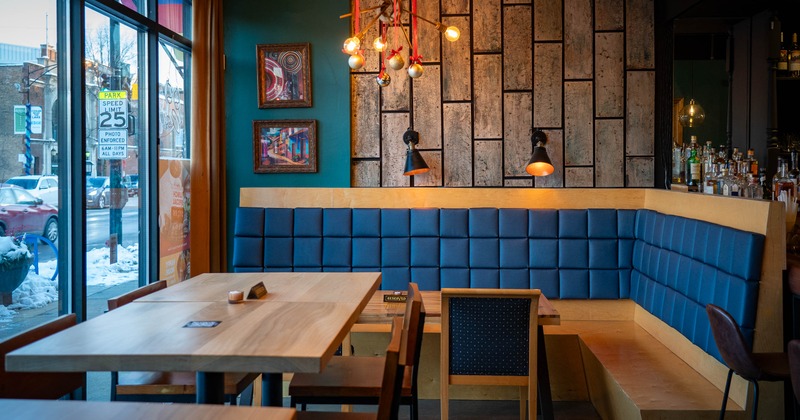 A cozy interior - wooden tables, blue upholstered booth seating and artwork on paneled walls