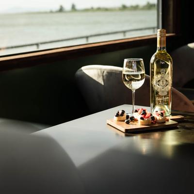 A view from inside showing the waterfront and a glass of wine with dessert.