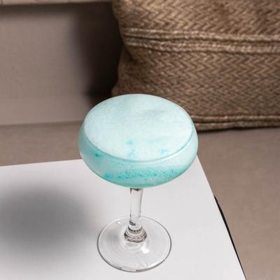 A coupe glass with a light blue cocktail drink.