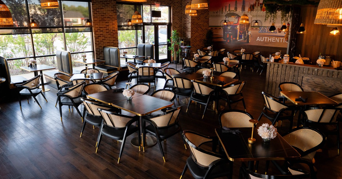 Warmly lit restaurant with wooden floors, black chairs, large windows, and wicker pendant lights