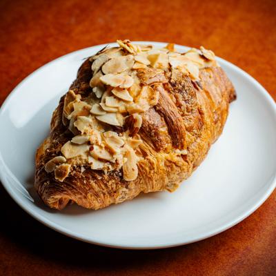 Croissant topped with sliced almonds, served on a white plate.