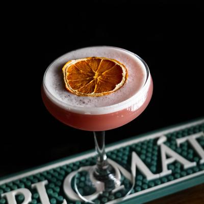 Pink cocktail served in a specialty glass with dry lemon wheel.