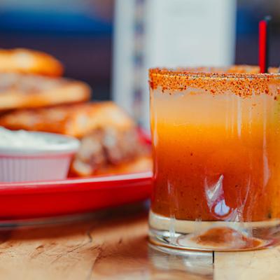Layered orange cocktail with chili rim and red straw.