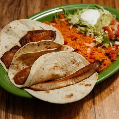Fish Tacos served with rice, guacamole, fresh salsa, and sour cream.