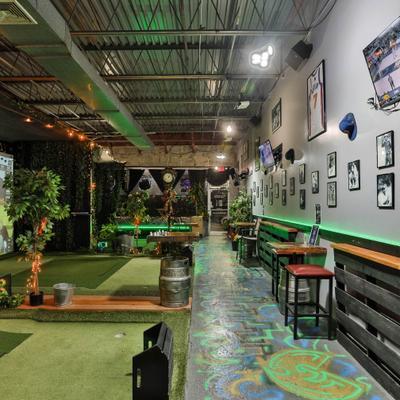 Indoor golf area with turf mats and neon lighting.
