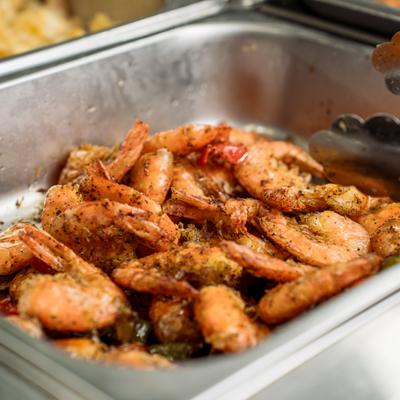 Seasoned cooked shrimp with tails on sit in a buffet warming pan.