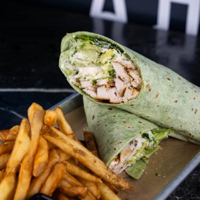 Chicken Caesar Wrap made with a spinach herb tortilla, served alongside fries.