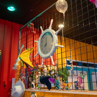 Nautical ship wheel clock hangs on metal mesh inside a colorful room.