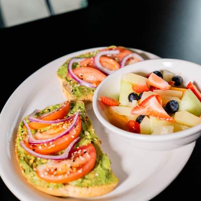 Avocado toast, served with a bowl of fresh fruits.