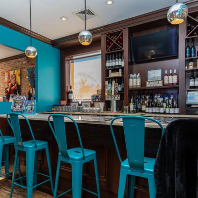 Bar with teal stools, wine and liquor bottles on shelves, and pendant lights.