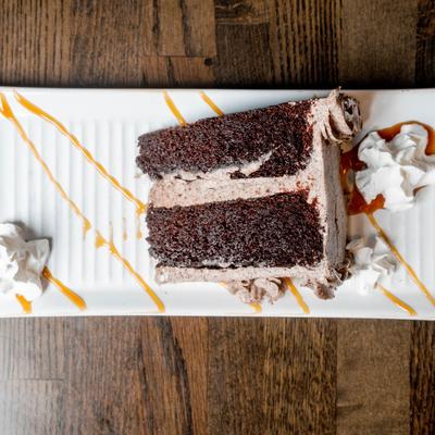 Oreo slice cake on a plate with whipped cream and caramel sauce drizzle.