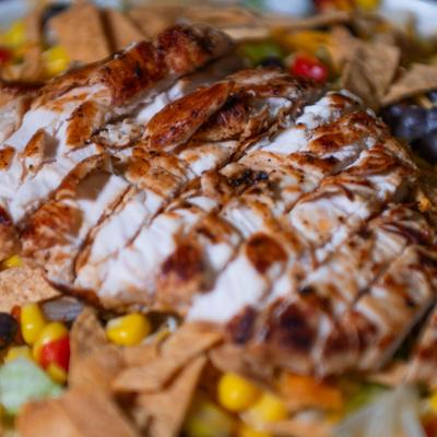 Sliced grilled chicken breast over corn, black beans, and tortilla strips.