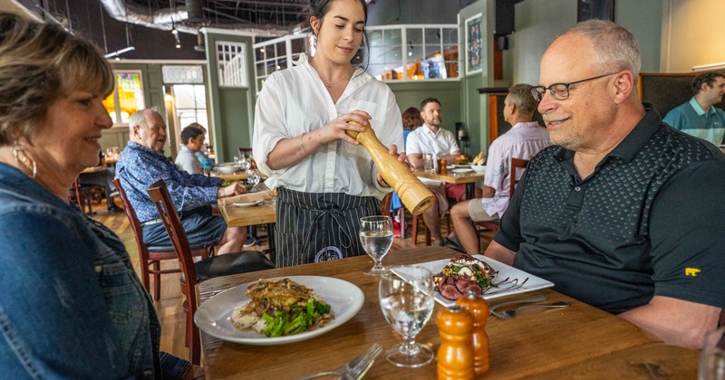Interior, a waiting staff member serving a couple