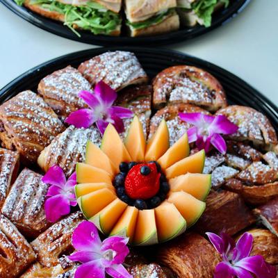 Puff pastry sandwiches on a platter with flower garnish and fruit arrangement