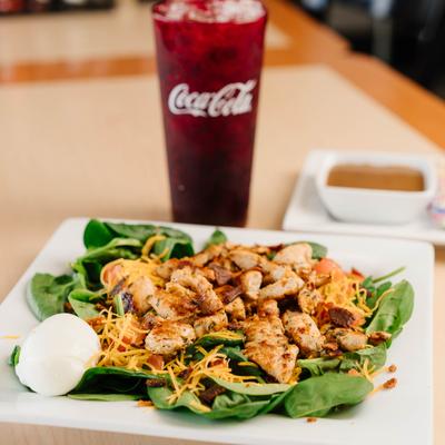 Grilled chicken salad with spinach, shredded cheese, and soft drink.