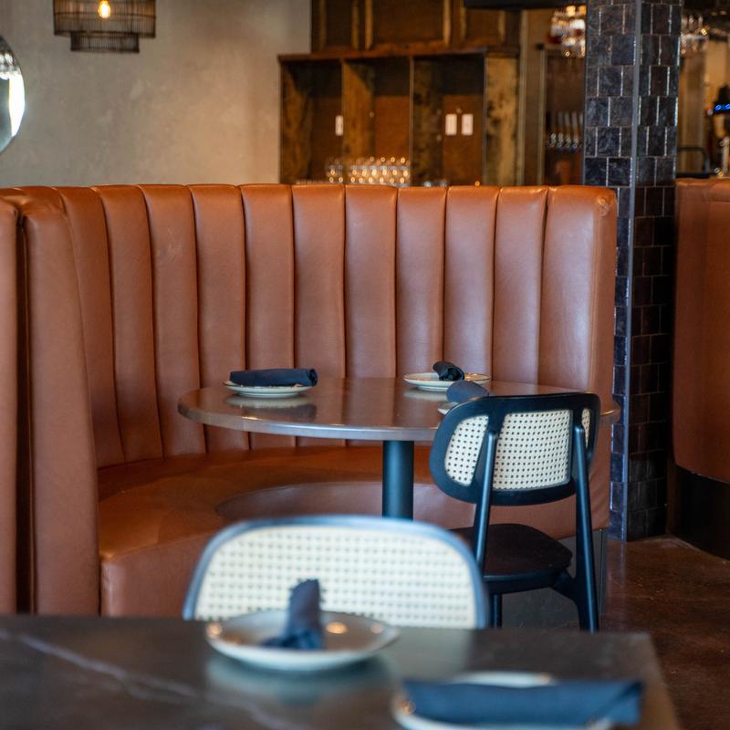 Curved brown leather booth with a round table and a woven back chair in a restaurant setting