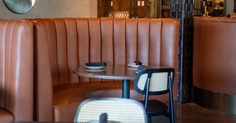 Curved brown leather booth with a round table and a woven back chair in a restaurant setting