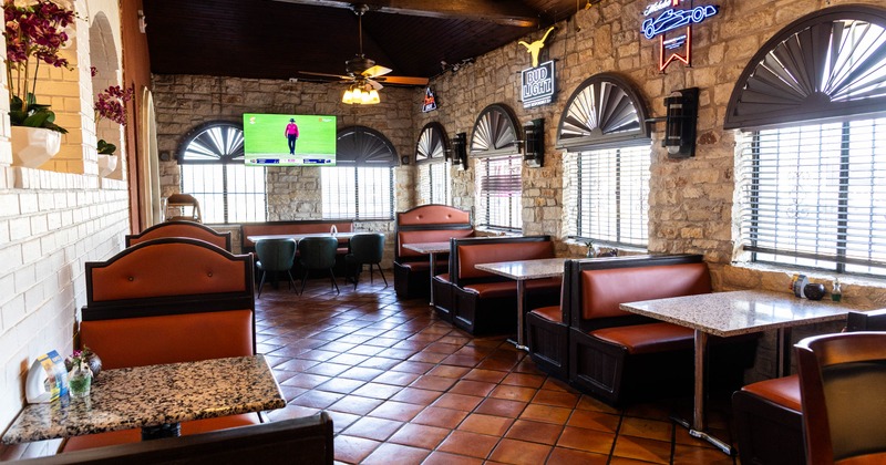 Rustic interior with booths, granite tables, stone walls and a TV showing a sports event