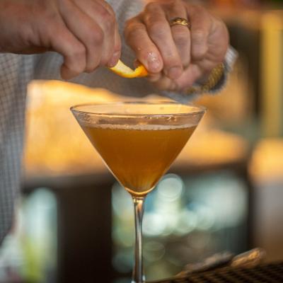 Plum cocktail in martini glass, garnished with a citrus twist.