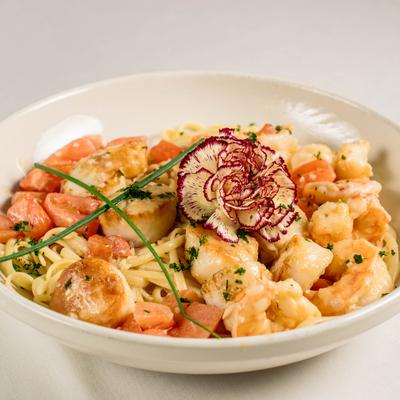 Creamy linguine pasta with shrimp, scallops, and chive and flower garnish.