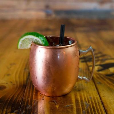 Cold drink in copper mug with lime wedge on a wooden table inside bar.