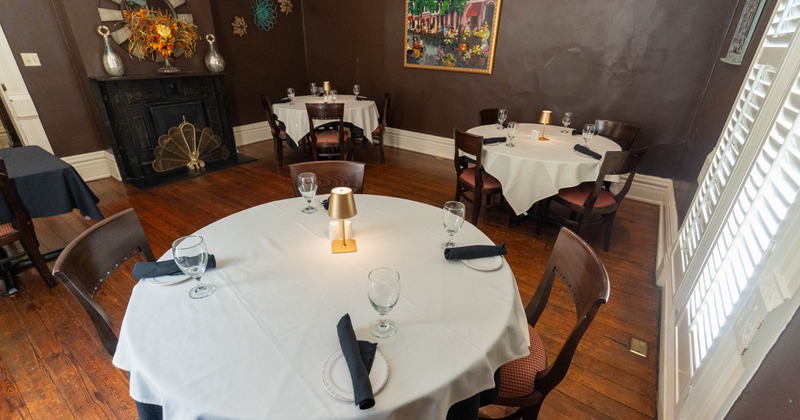 An elegant dining room with white tableclothed tables, set with glassware and black napkins