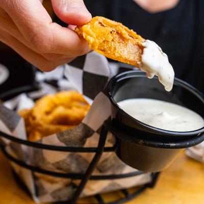 A person dips an onion ring into a sauce.