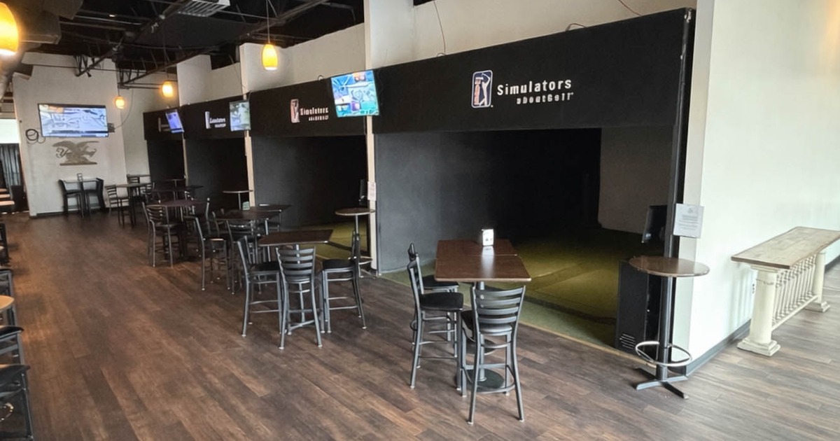 Open interior with simulator bays, wood flooring, and high dining tables