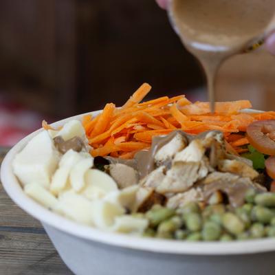 Salad with grilled chicken being topped with a dressing.