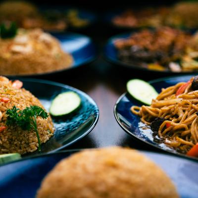 Plates of fried rice and noodles with cucumber slices on a table.