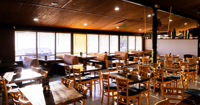 Spacious restaurant interior with wooden tables, chairs, and booth seating near large windows