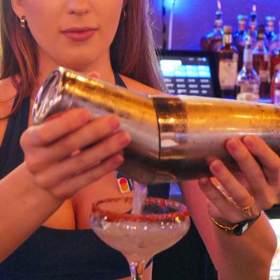 A bartender pouring a cocktail from a shaker into a coupe glass.