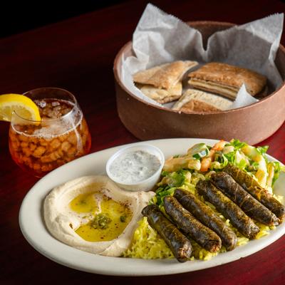 Meat grape leaves, dip, tzatziki, rice and salad on a plate, a glass of ice tea, pita bread.