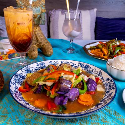 Stir-fry purple eggplant and colorful vegetables, served alongside a glass of Thai iced tea.
