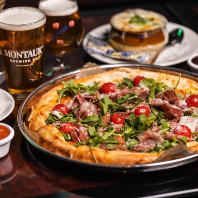 Prosciutto and arugula pizza with cherry tomatoes served with a pint of beer.