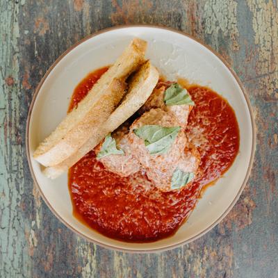 Meatballs with red sauce, Parmesan, basil, and crostini on a plate.