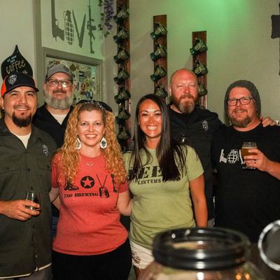 A group of six people smiling at the brewery, holding beer glasses.