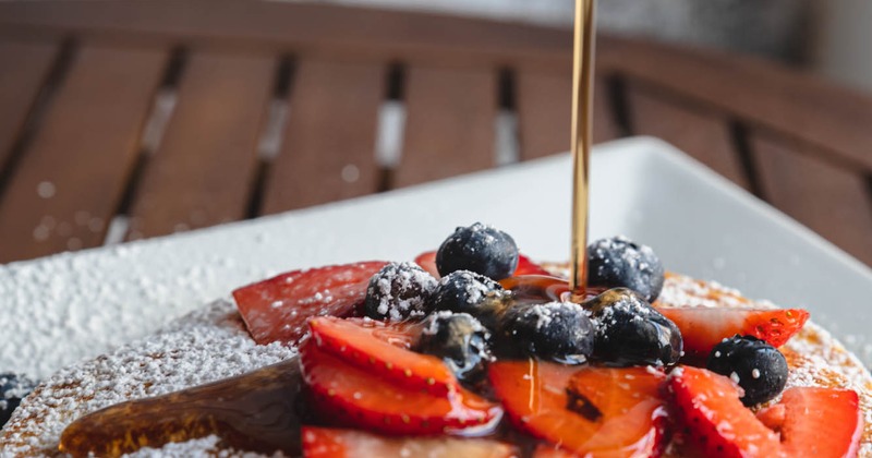 Pancakes topped with powdered sugar, syrup and berries, closeup
