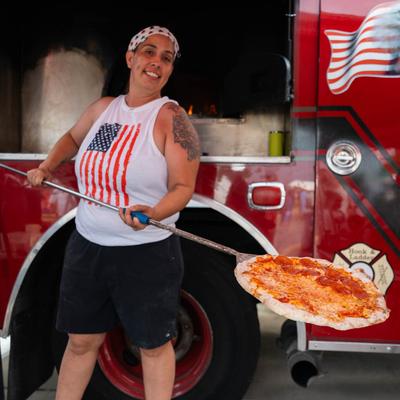 A food truck worker holding a half-cheese, half-pepperoni pizza on a peel.