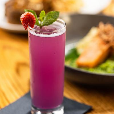 Purple cocktail in a tall glass, garnished with mint and a strawberry.