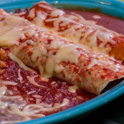 Enchiladas topped with melted cheese in red sauce.