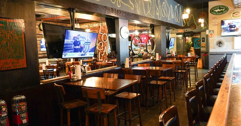 Interior view of a cozy restaurant featuring wooden tables and chairs, a bar, mounted TVs