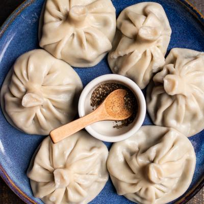 georgian soup dumplings (khinkali) on blue plate, with ramekin of ground pepper